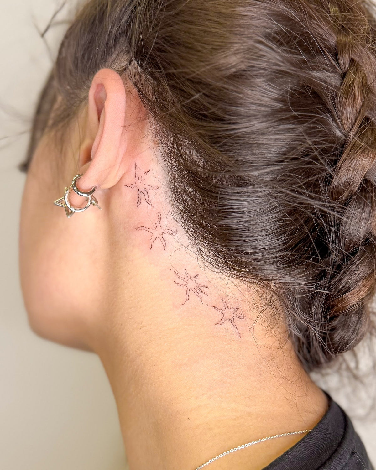 Fine line tattoo of little stars trailing behind the ear and down the neck, by Eli Inking in Bristol