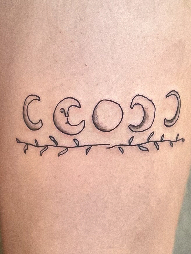 Fine line moon phases tattoo with a leafy vine on the back of a thigh, by Eli Inking, Bristol