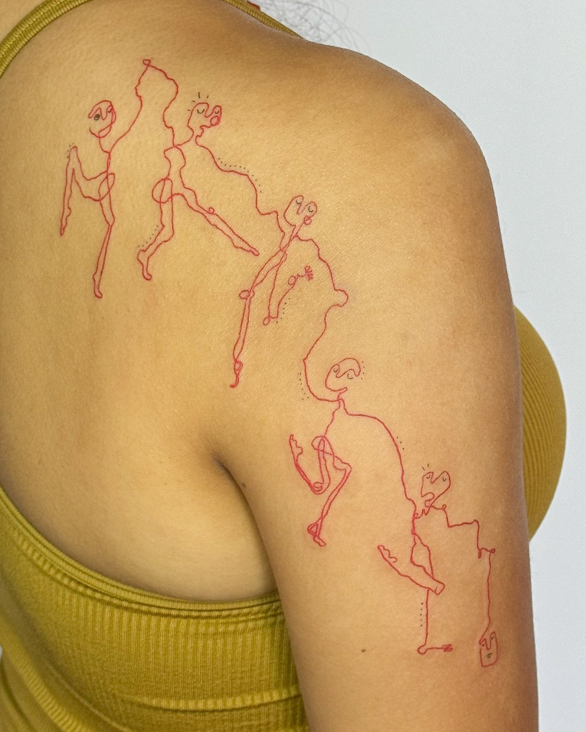 Red fine line tattoo of little figures dancing across the shoulder and upper back, by Eli Inking in Bristol