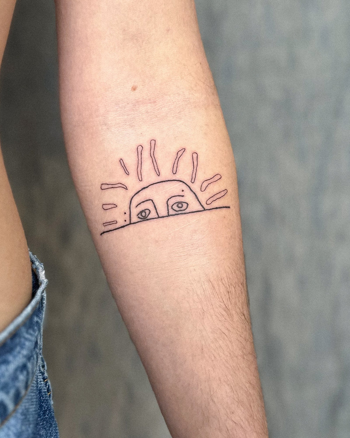 Fine line rising sun tattoo with eyes peeking over the horizon on the forearm, by Eli Inking