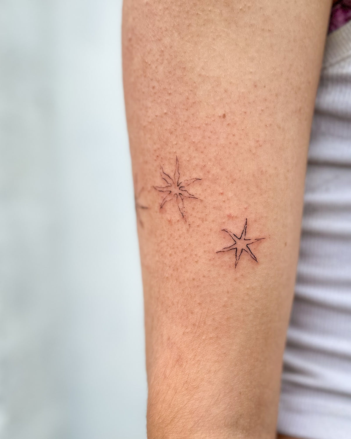 Fine line tattoo of two small sparkle stars, on the arm, by Eli Inking in Bristol