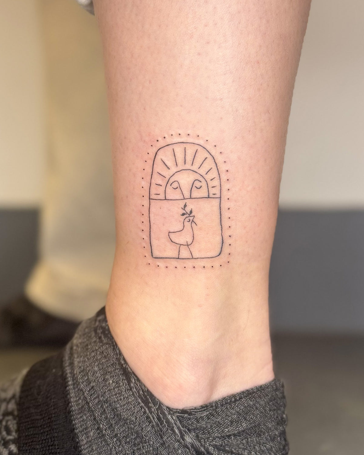 Fine line tattoo of a little sun and figure inside a dotted arch, on the calf, by Eli Inking in Bristol