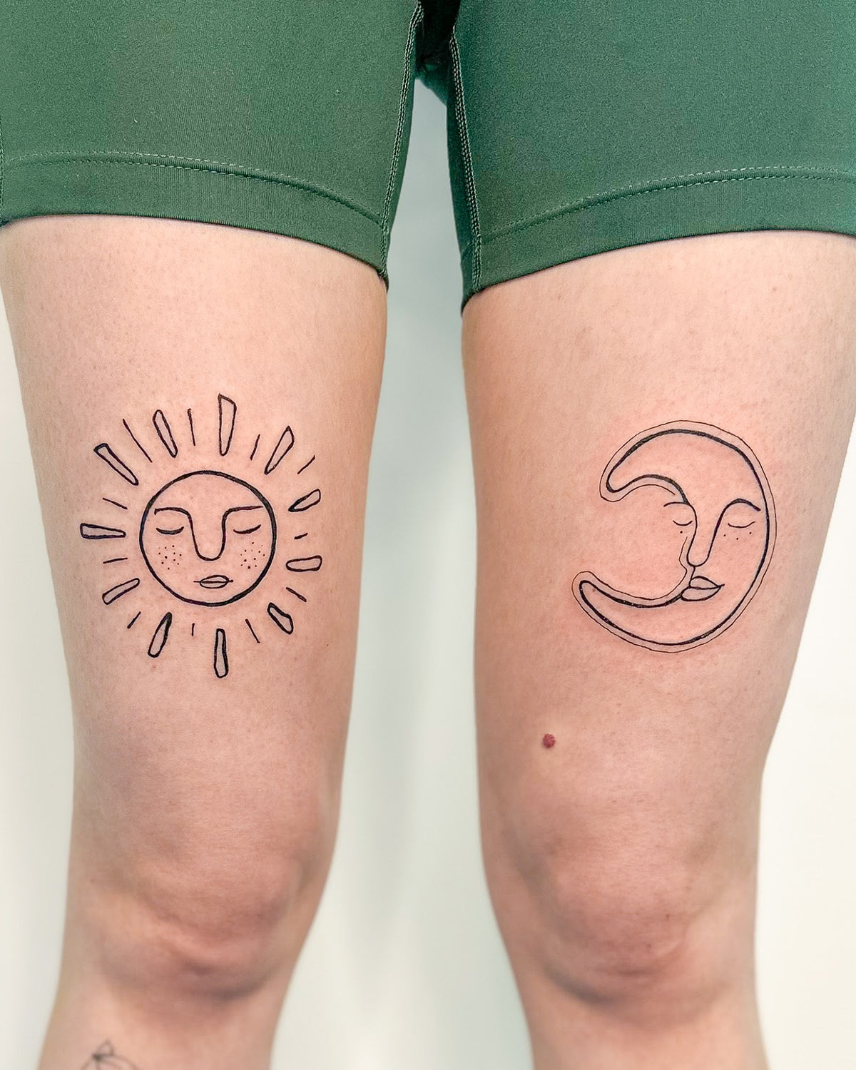 Matching fine line sun and moon tattoos, one above each knee, by Eli Inking