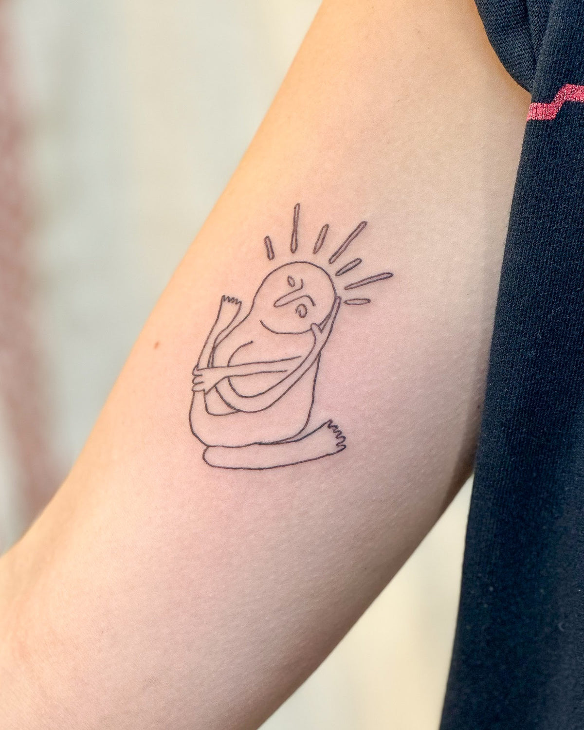 Fine line seated figure with a sunburst for a head on the upper arm, by Eli Inking