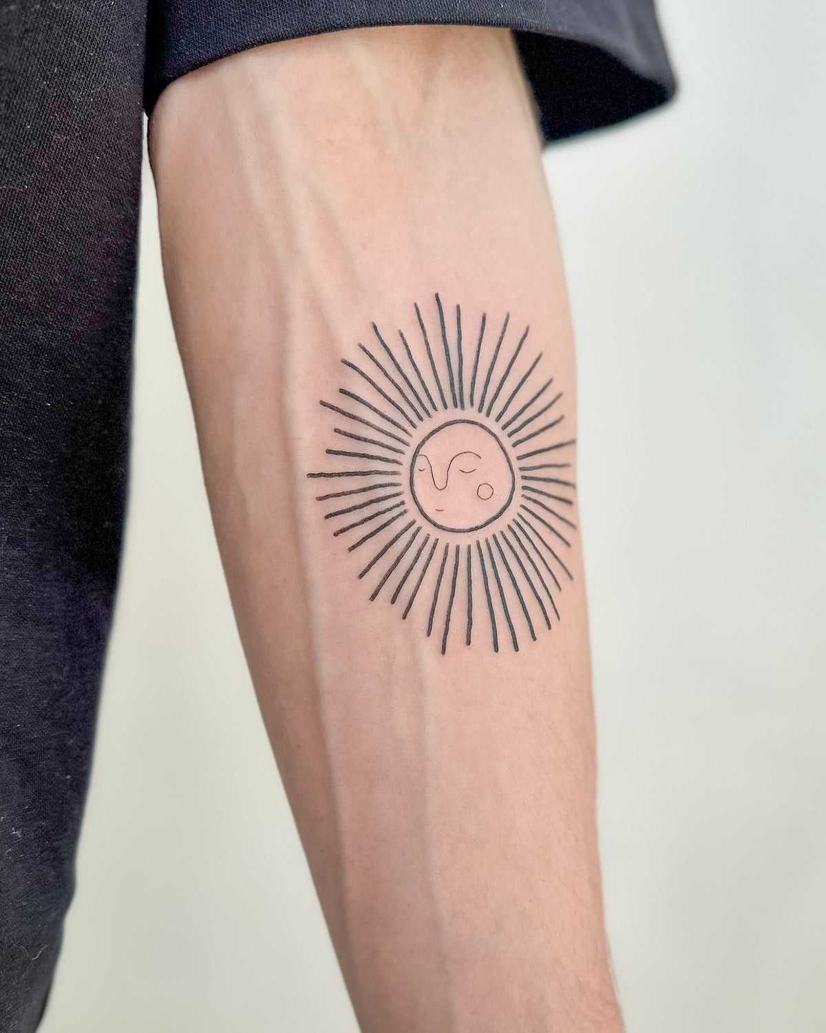 Fine line sunburst tattoo with long thin rays on the forearm, by Eli Inking