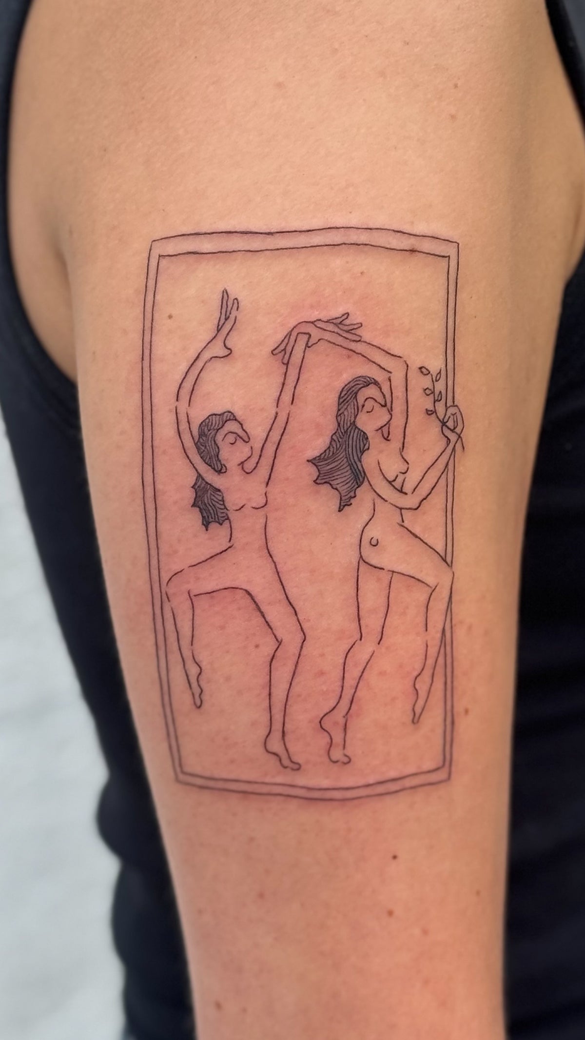 Fine line tattoo of two women dancing inside a tall frame, on the upper arm, by Eli Inking in Bristol