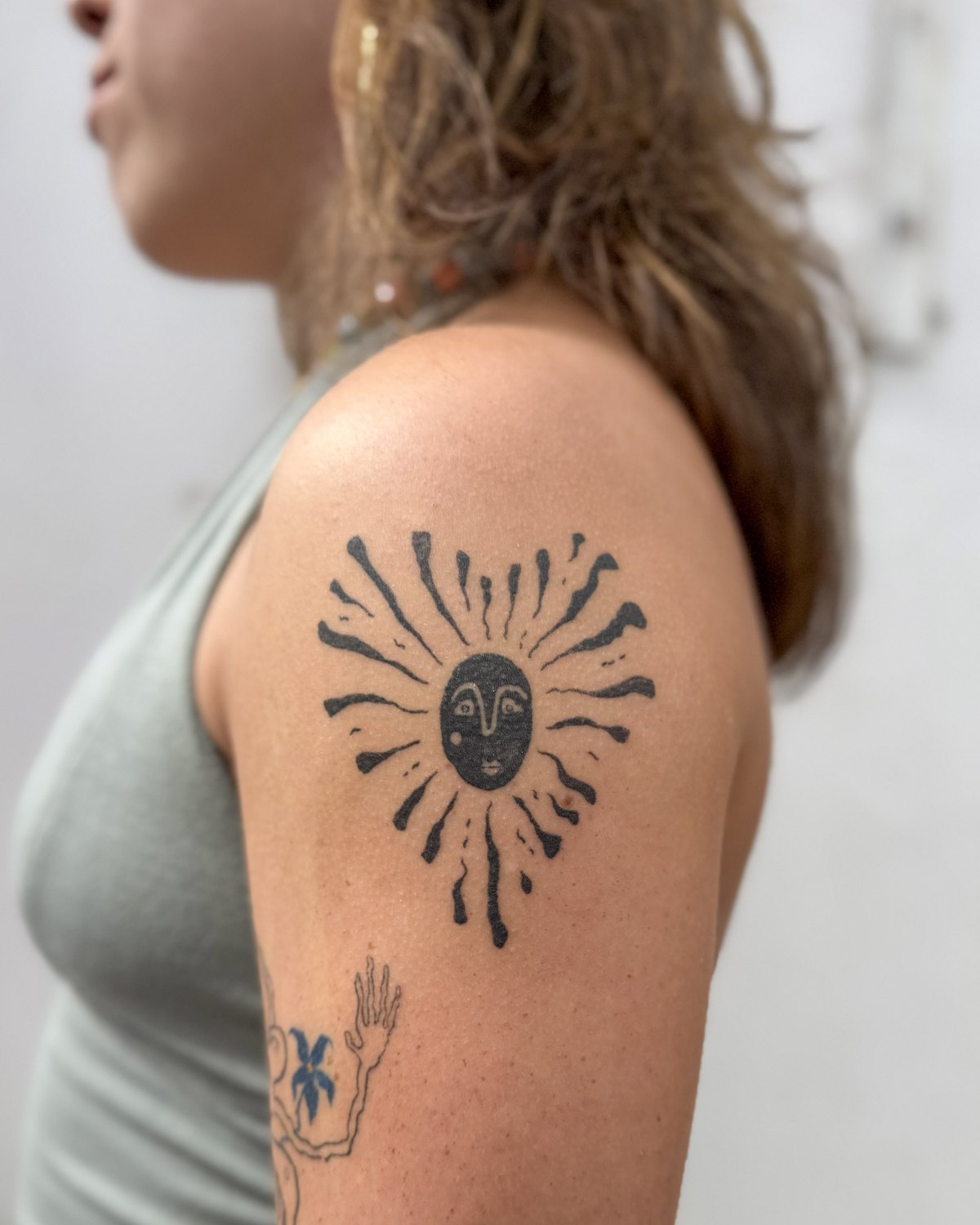Healed tattoo of a bold black sun with a face, on an upper arm