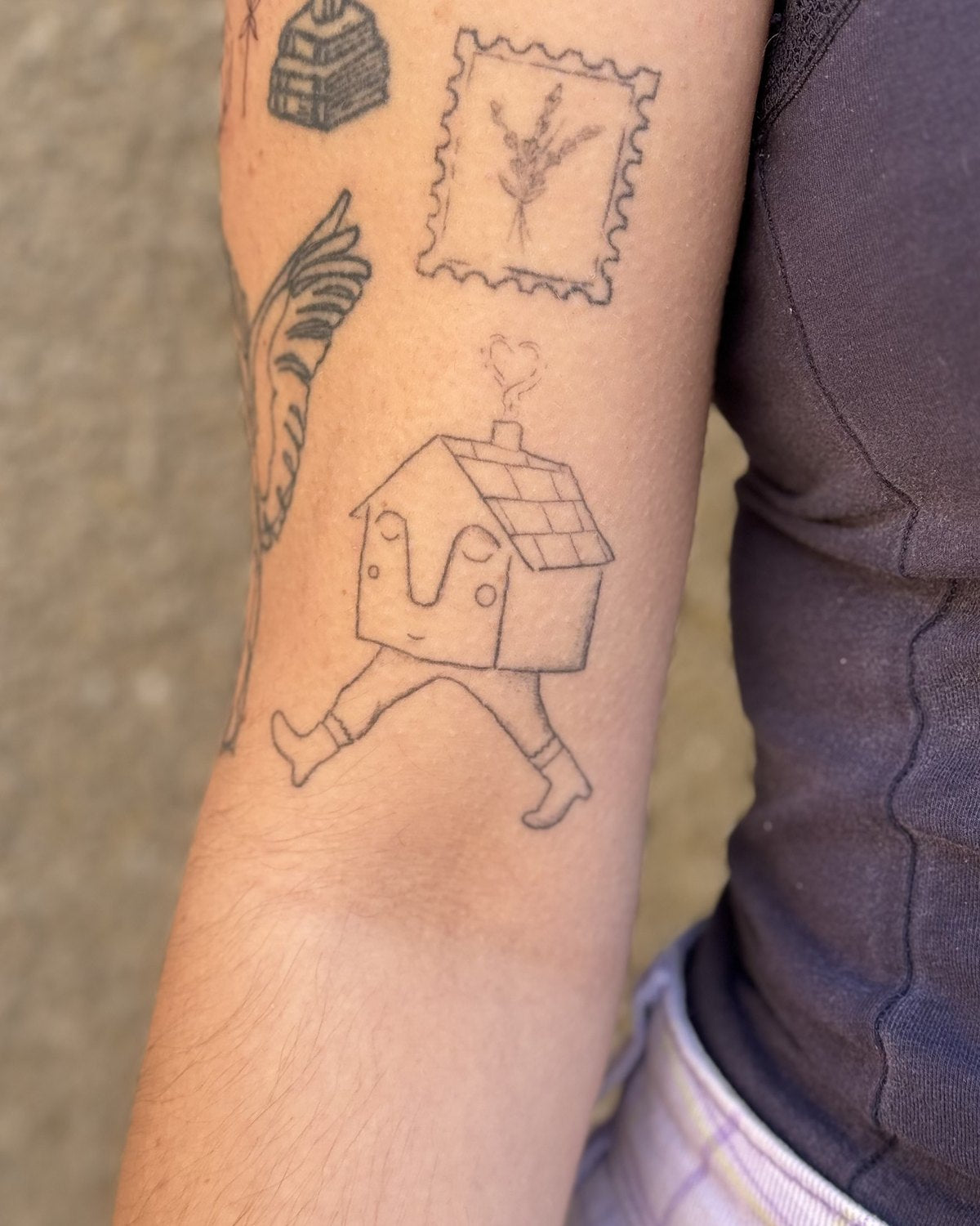 Healed fine line tattoos on an arm, including a walking house, a beehive and a framed panel