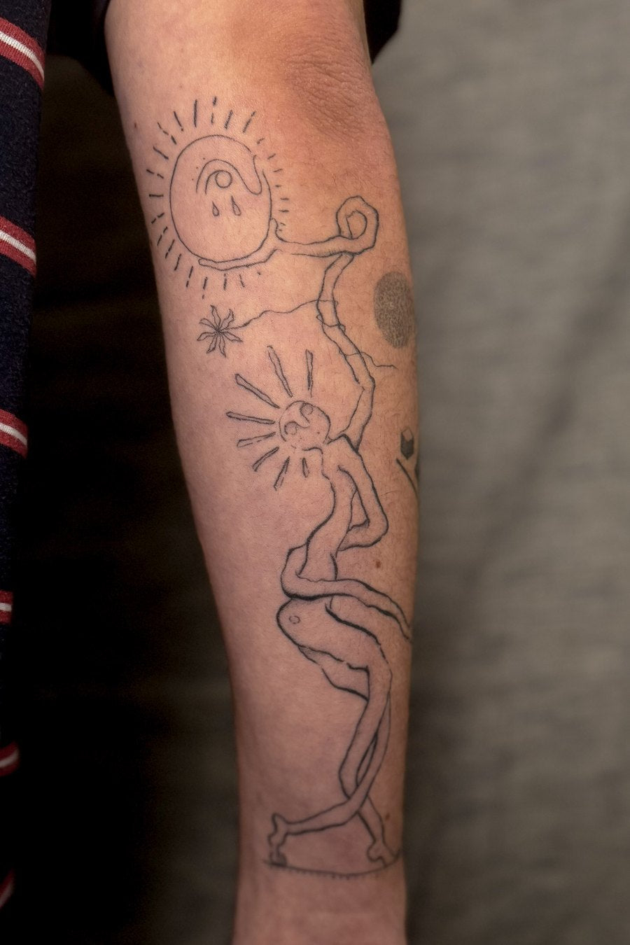 Healed forearm tattoo of a figure and a sun with grey wash shading