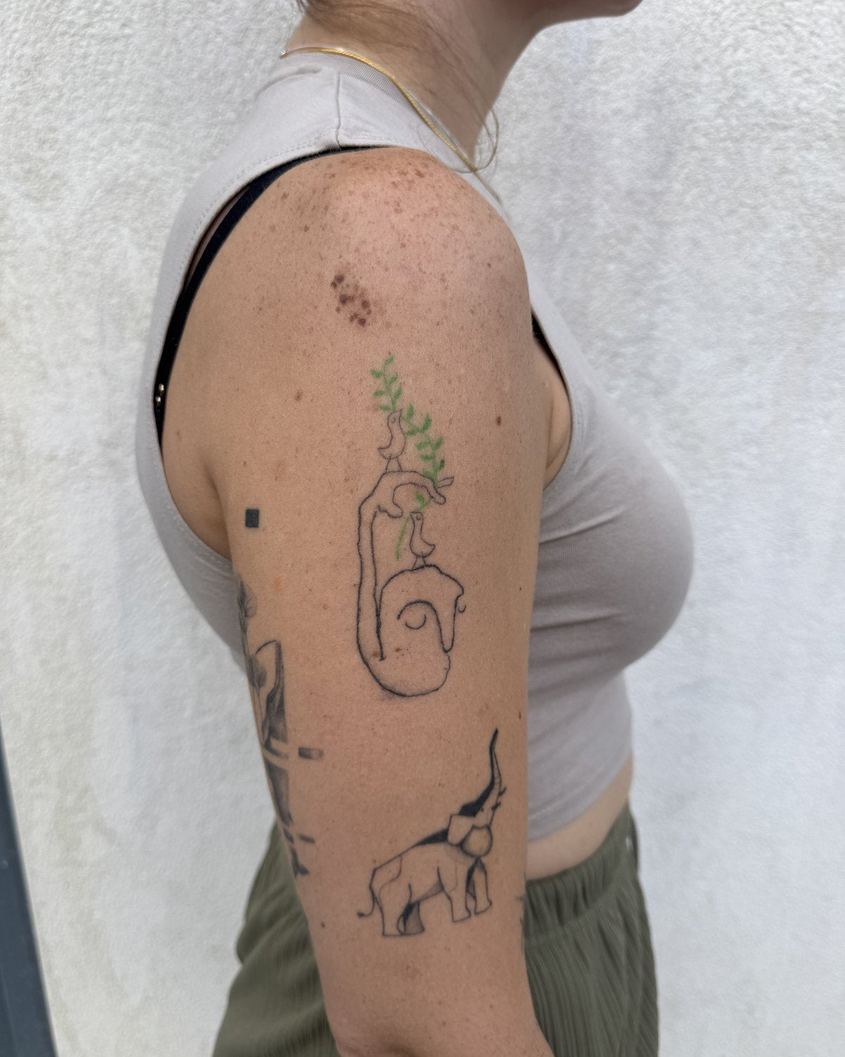 Healed tattoo of a head with a green leaf growing from it, on an upper arm