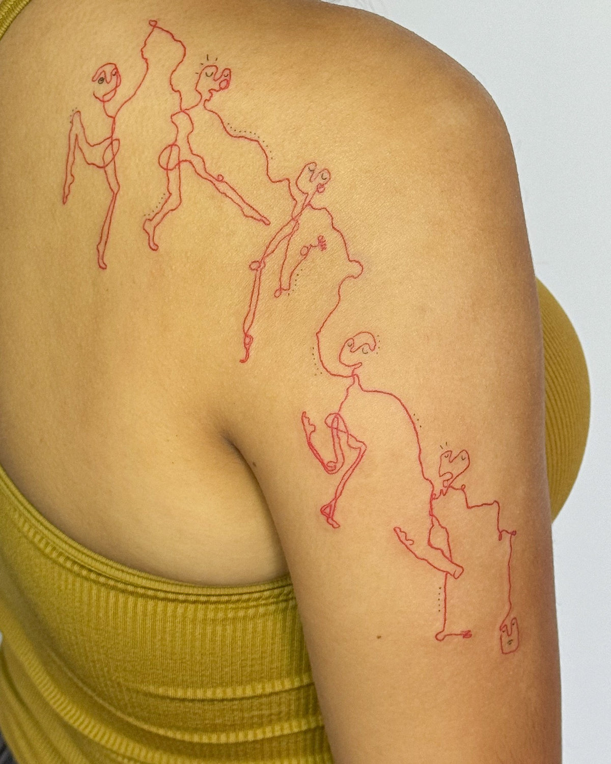 Red line tattoo of dancing figures tumbling over the shoulder and down the arm, by Eli Inking in Bristol