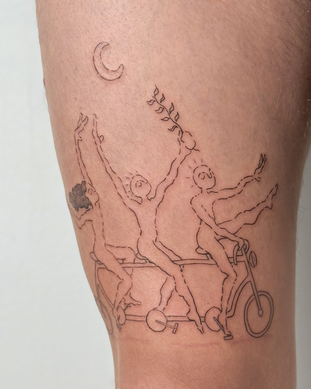 Large fine line thigh tattoo of three figures riding a tandem bike under a crescent moon, by Eli Inking in Bristol