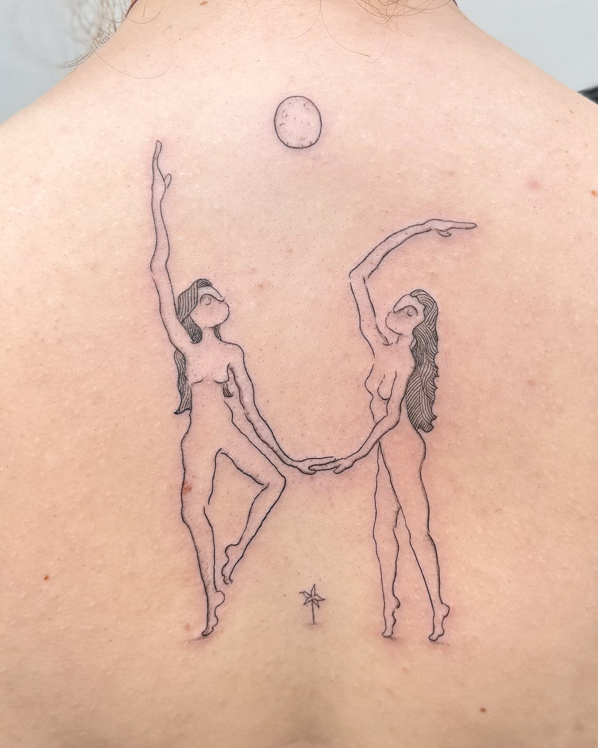 Fine line back tattoo of two women dancing hand in hand up towards the sun, by Eli Inking in Bristol