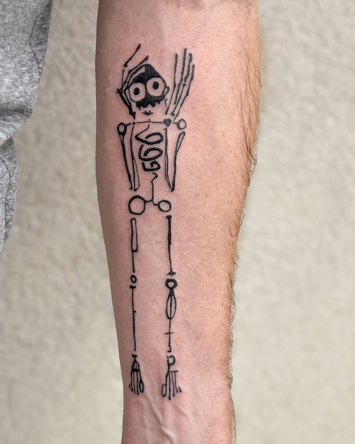 A long skeleton tattoo with spiral ribs and big eyes, waving, down a forearm, by Eli Inking