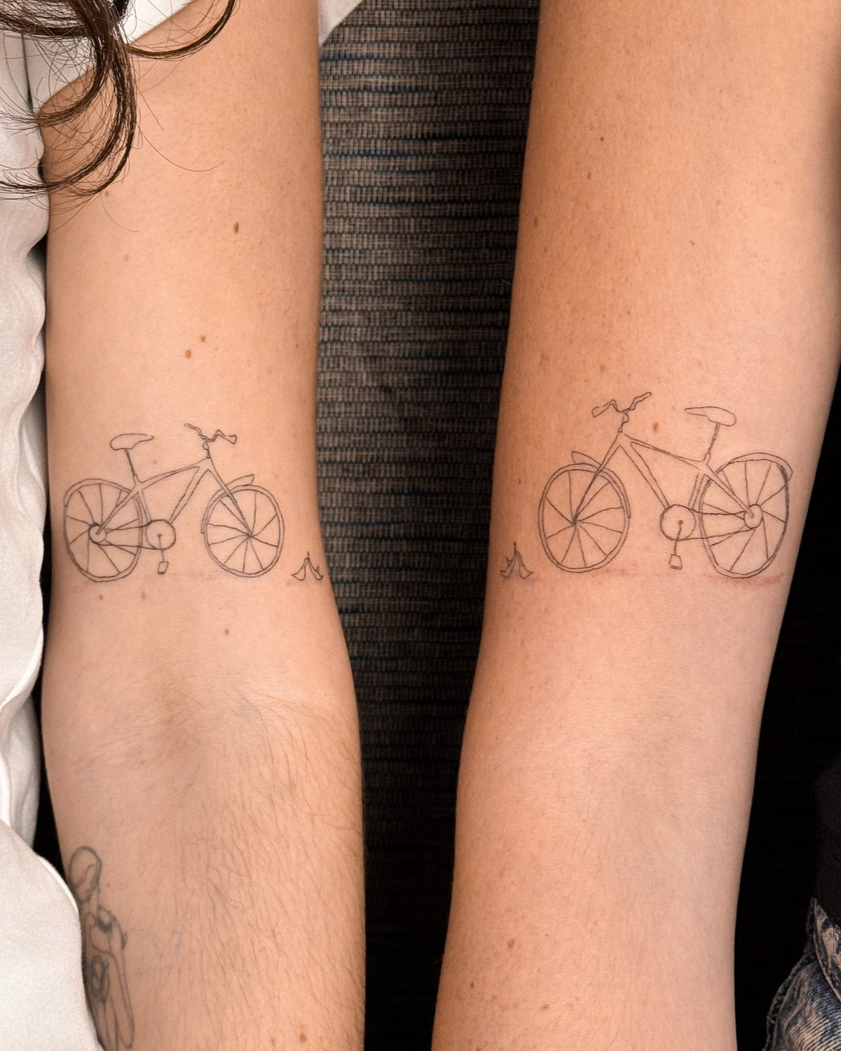 Matching fine line bicycle tattoos on two people's forearms, by Eli Inking in Bristol