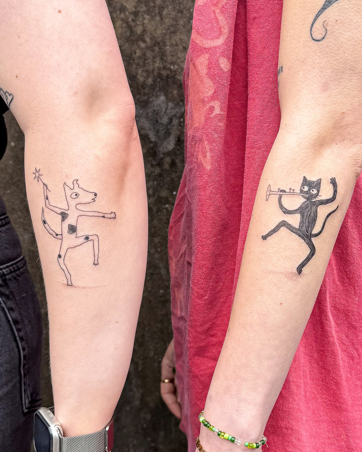 Two tattoos made as a pair: a dancing dog and a dancing cat playing a trumpet, on two people's forearms, by Eli Inking in Bristol