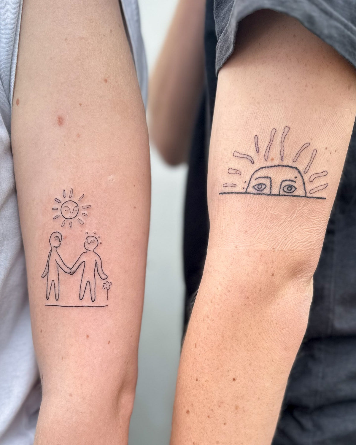 Two tattoos made as a pair: two figures holding hands under a sun, and a sun peeking over the horizon, by Eli Inking in Bristol