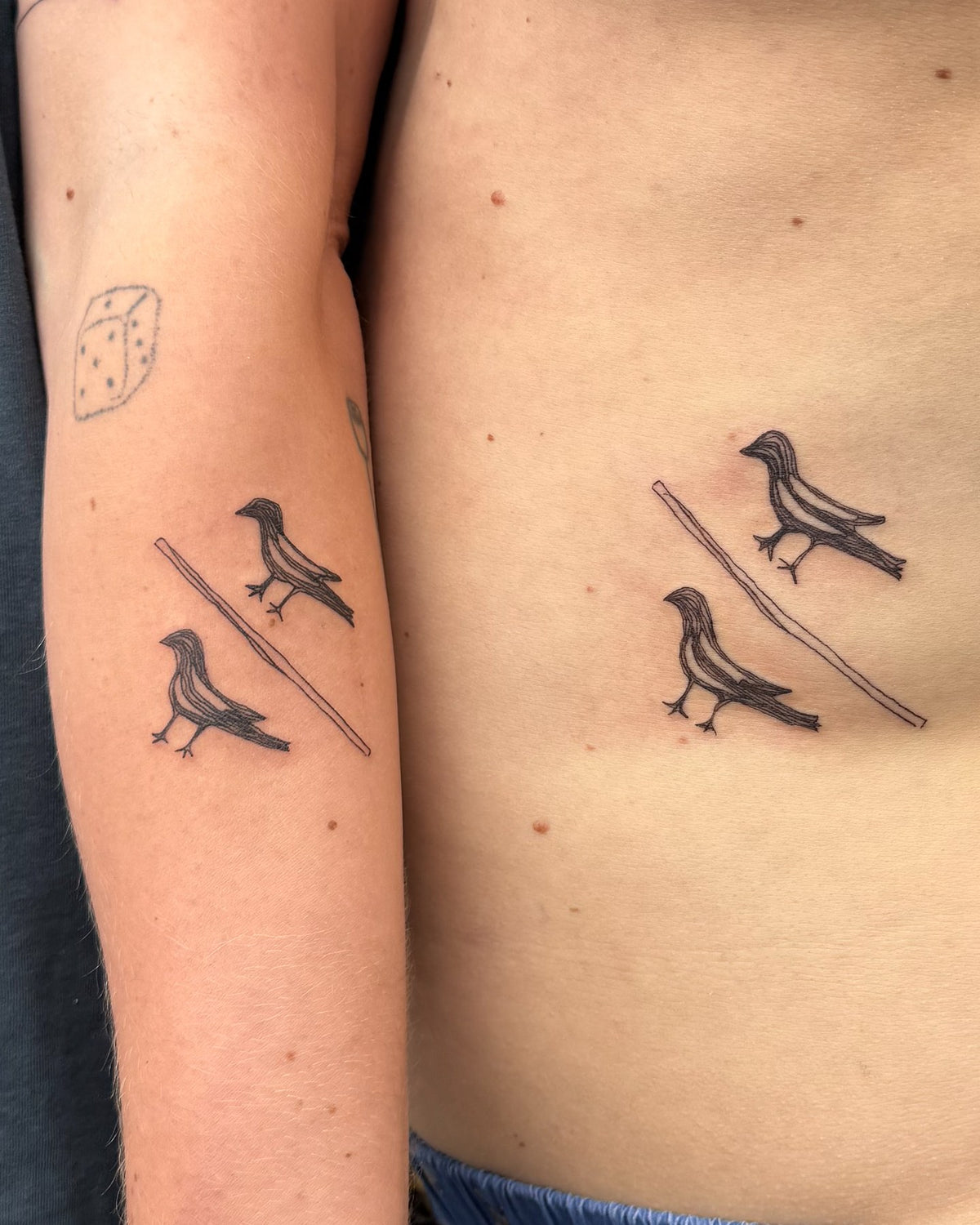 Matching tattoos of two magpies on a wire, on one person's forearm and another's ribs, by Eli Inking in Bristol