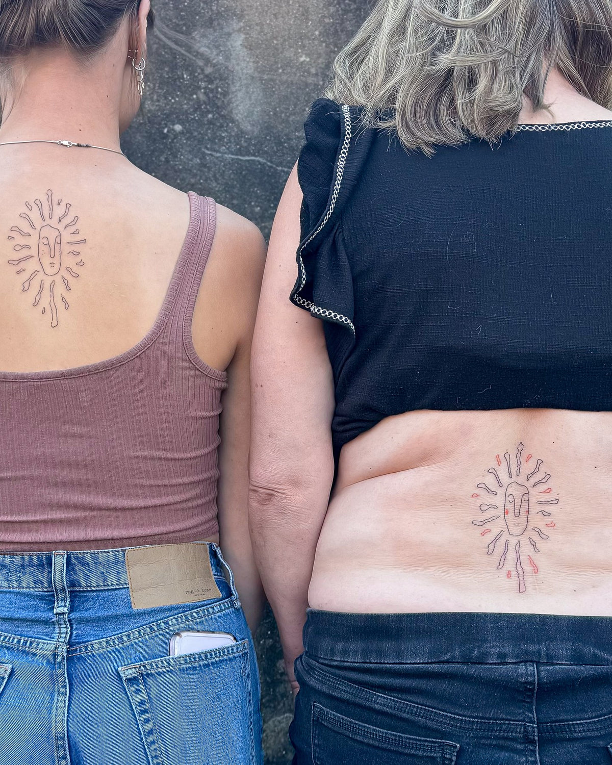Two people with matching fine line sun tattoos on the spine, one on the upper back and one on the lower back, by Eli Inking in Bristol