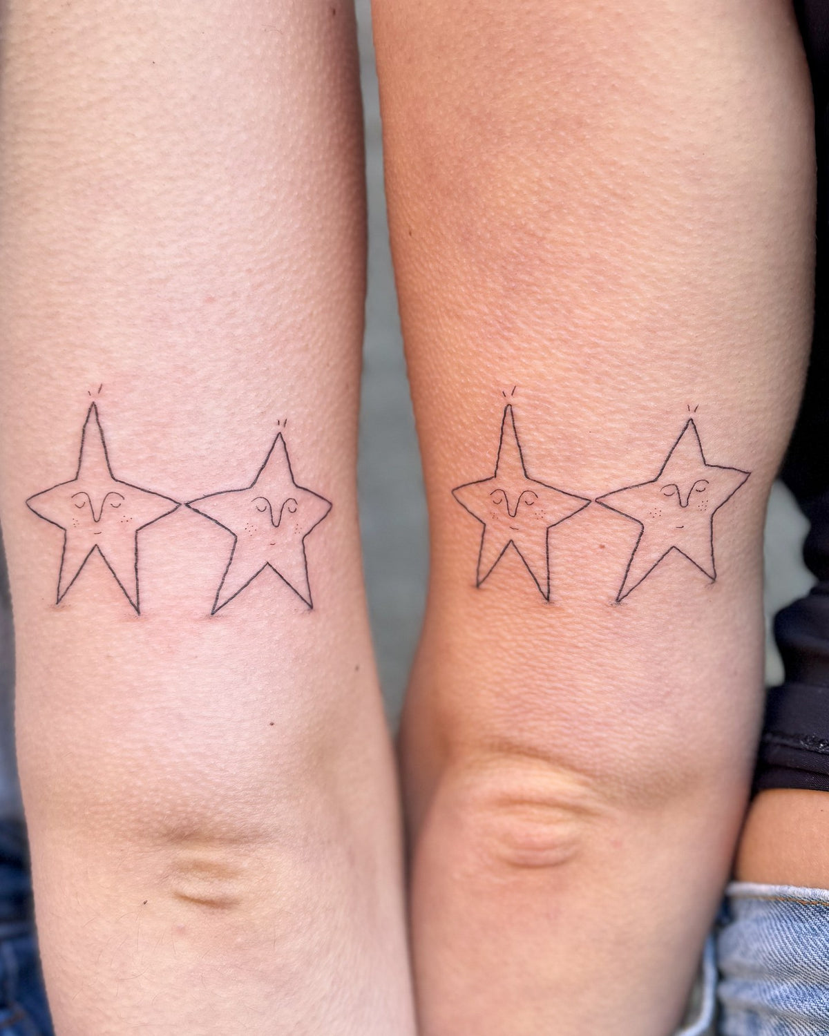 Matching tattoos of two little stars with faces on the backs of two people's arms, by Eli Inking in Bristol