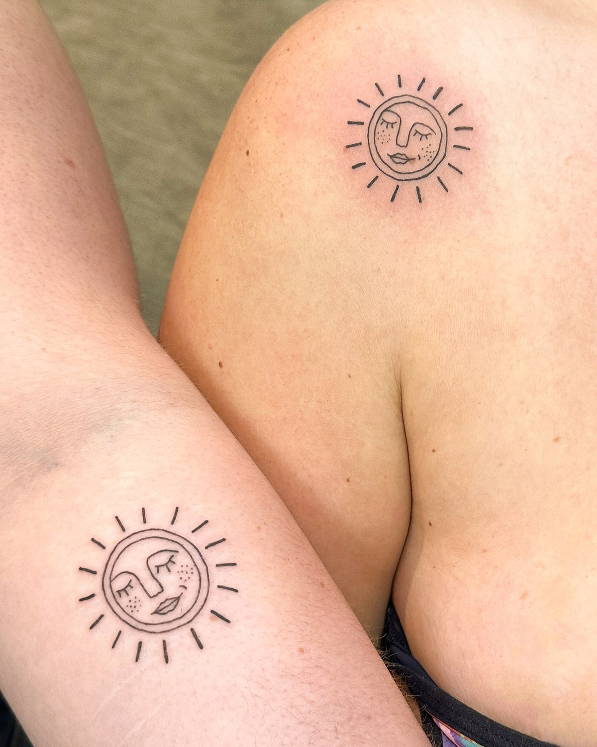Matching fine line sun face tattoos, one on a forearm and one on a shoulder, by Eli Inking in Bristol
