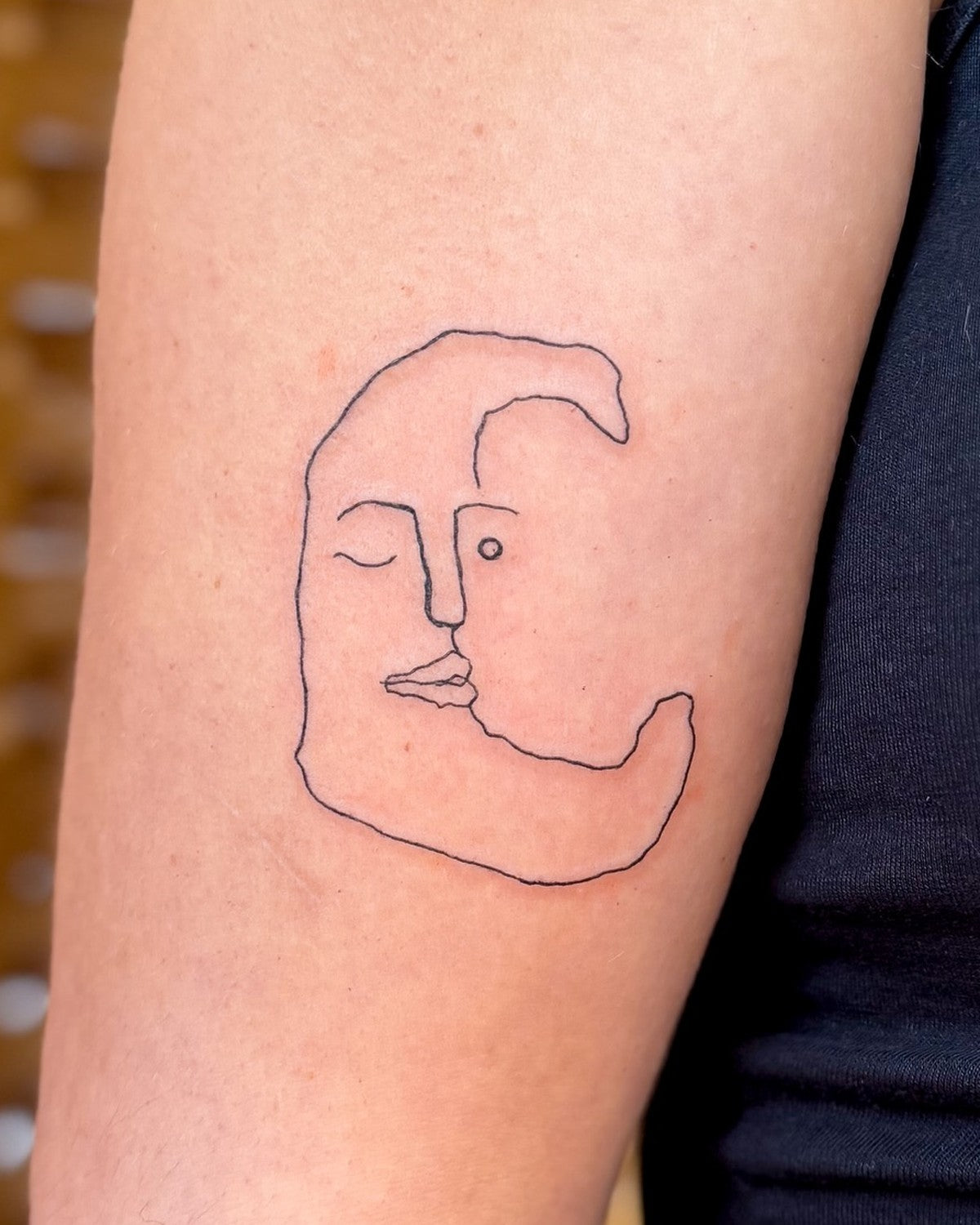 Fine line crescent moon tattoo with a sleeping face, close up on the arm, by Eli Inking, Bristol