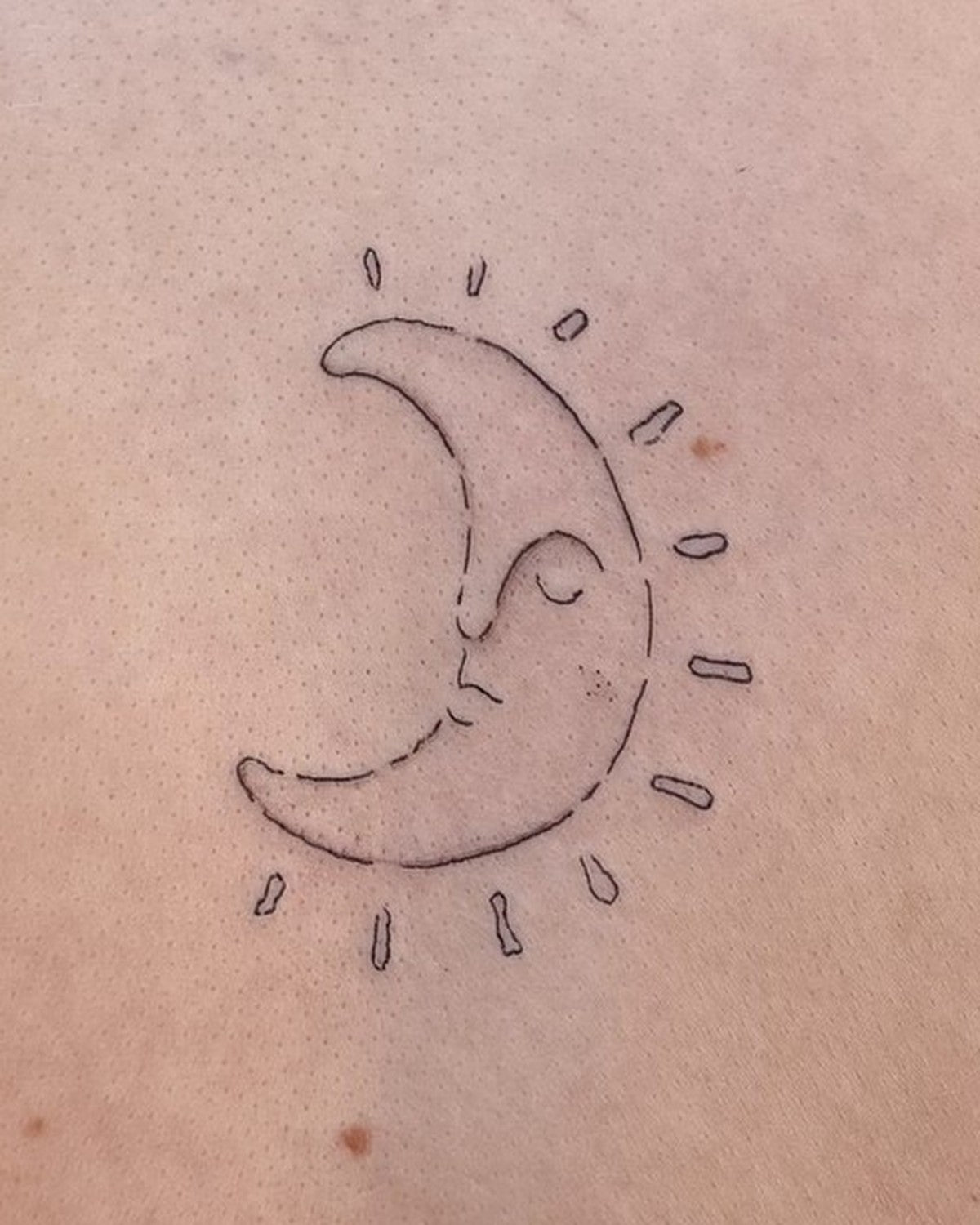 Small fine line crescent moon face tattoo with rays, close up on the upper back, by Eli Inking, Bristol
