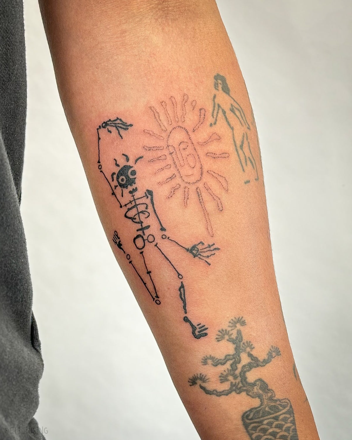Skeleton and sun tattooed on a forearm, redrawn to fit around healed tattoos by other artists