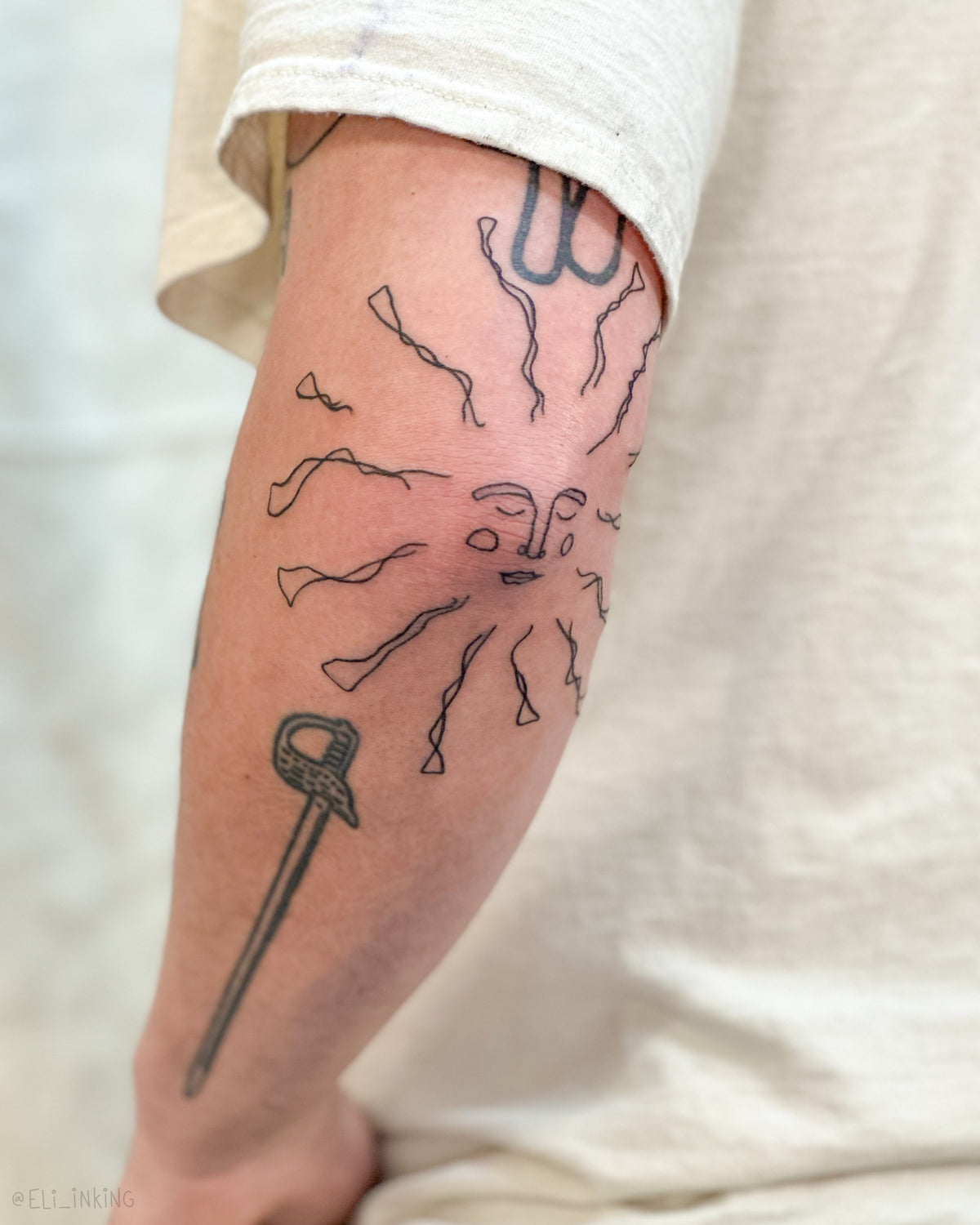 Close-up of a freehand sun tattooed at the elbow, drawn to link the tattoos either side