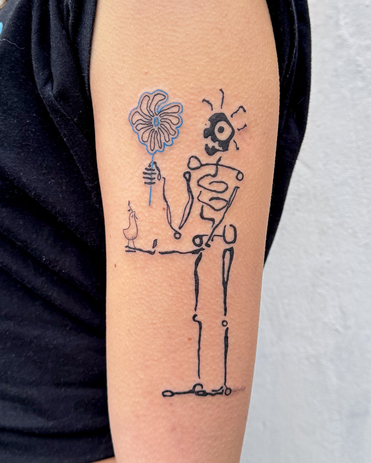 A skeleton tattoo with spiral ribs holding up a big blue flower, on an arm, by Eli Inking