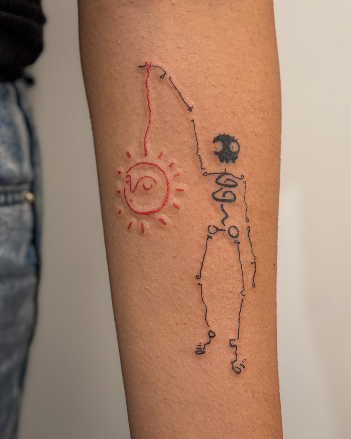 Skeleton tattoo fishing, with a red sun hanging on the end of its line, on a forearm, by Eli Inking in Bristol