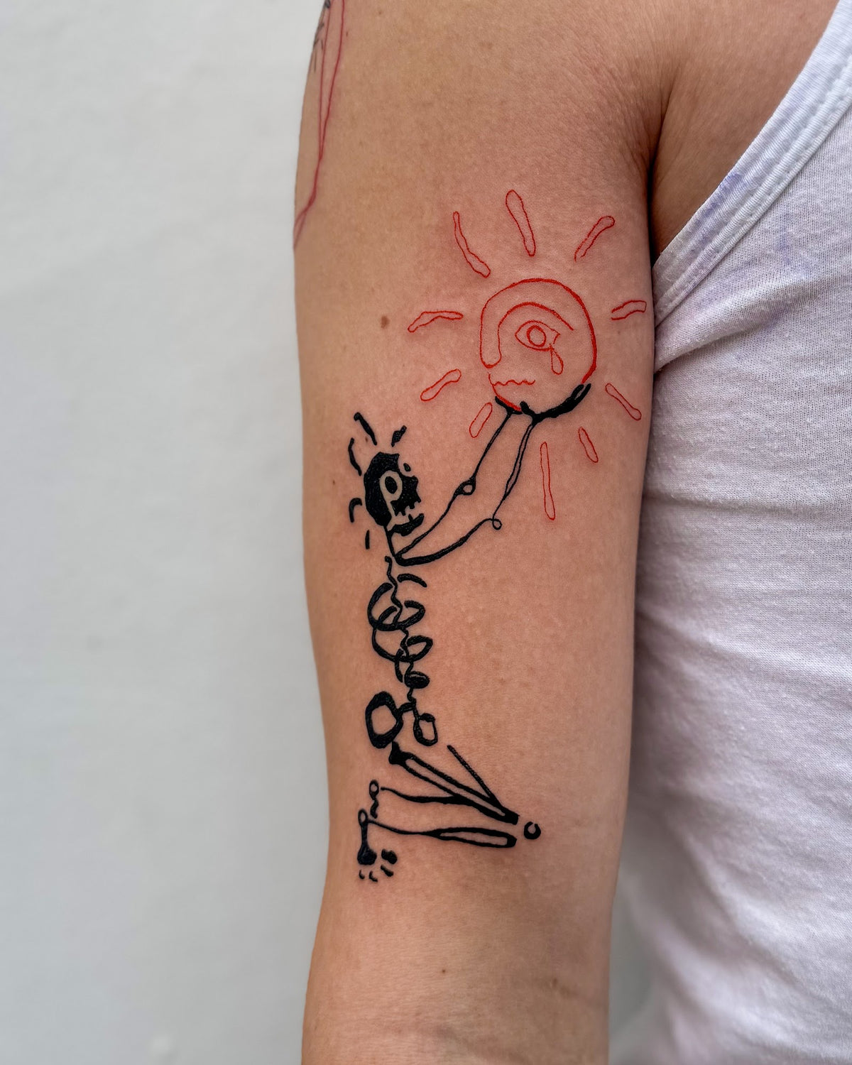 Bold black skeleton tattoo holding up a big red line sun on the back of an arm, by Eli Inking in Bristol