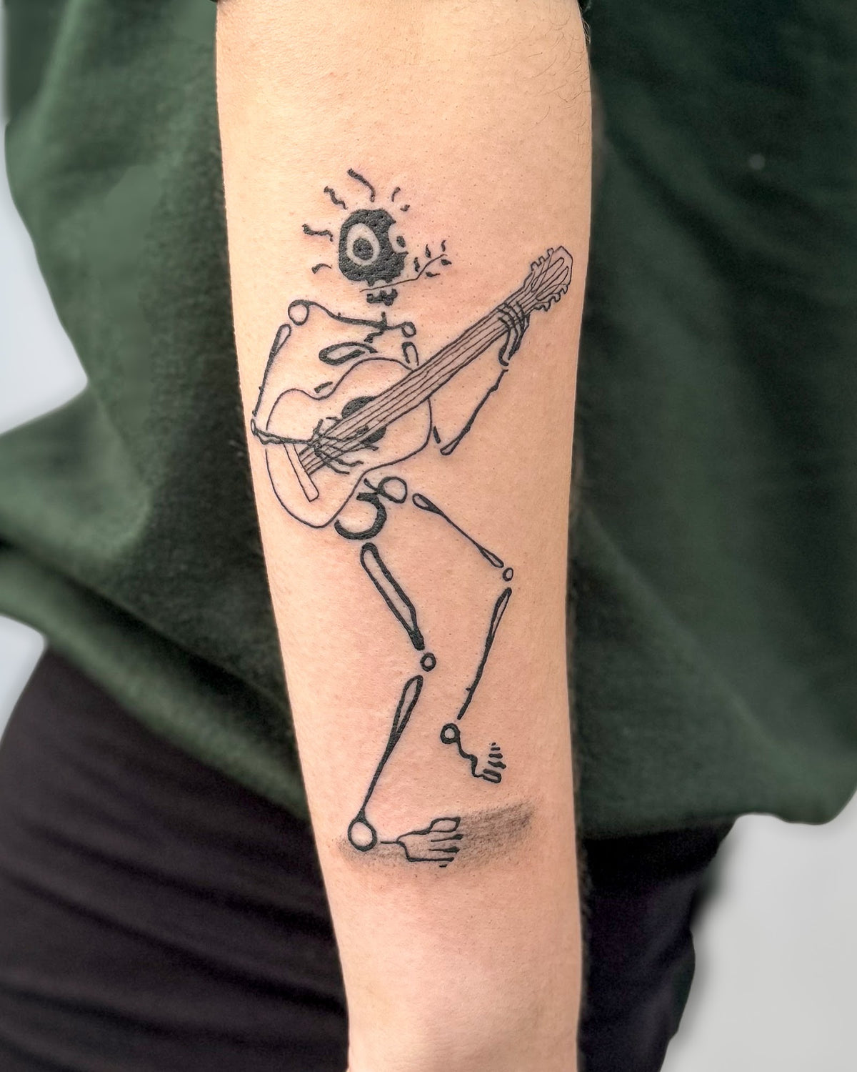Skeleton tattoo playing an acoustic guitar mid step, on a forearm, by Eli Inking in Bristol