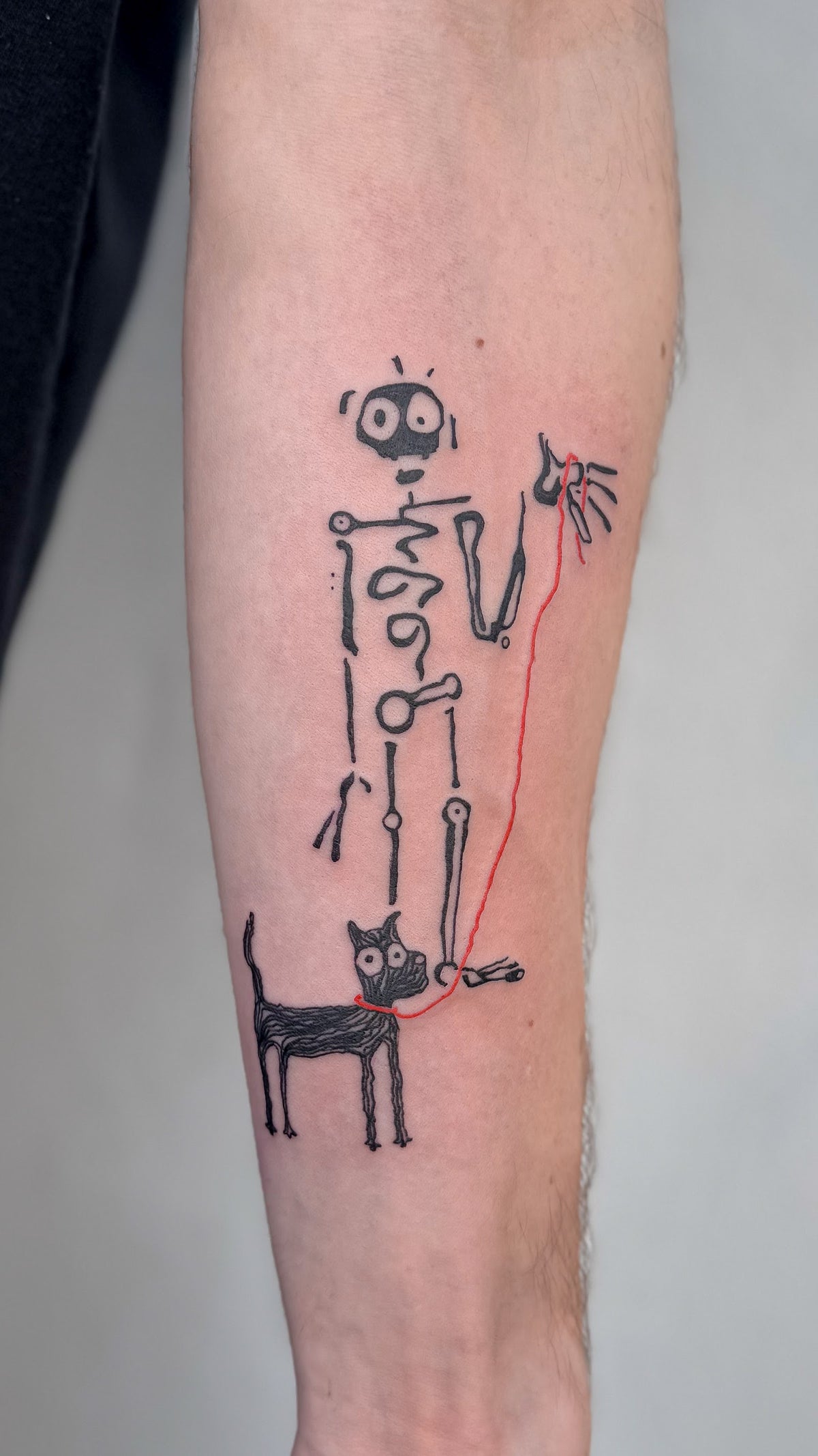 Skeleton tattoo walking a little black dog on a red lead, on a forearm, by Eli Inking in Bristol