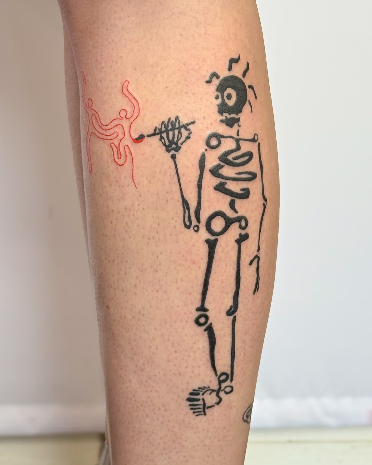 A bold skeleton tattoo with spiral ribs holding out a wiggly red flower, on a calf, by Eli Inking