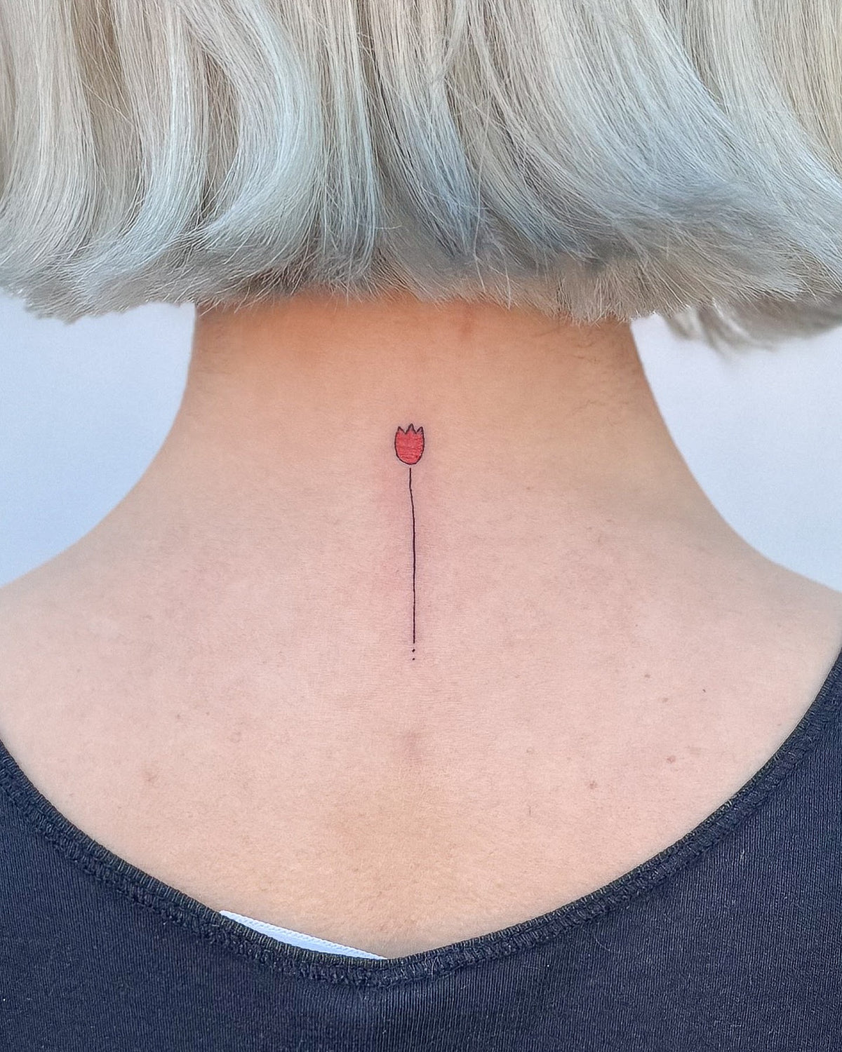 Tiny red tulip tattoo on a long thin stem, down the back of the neck, by Eli Inking, Bristol