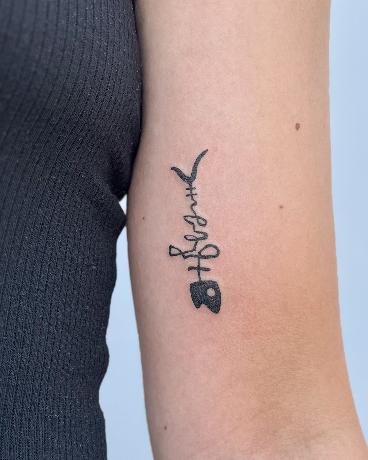 Small bold black tattoo of a column of tiny symbols, on the upper arm, by Eli Inking, Bristol
