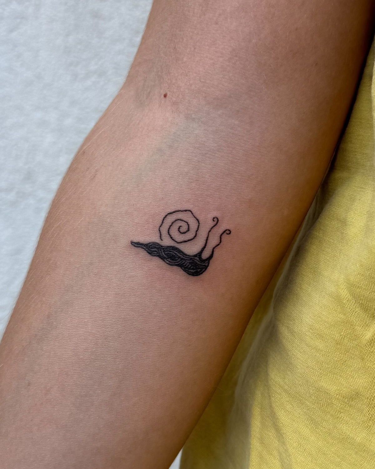 Tiny black snail tattoo on the forearm by Eli Inking in Bristol