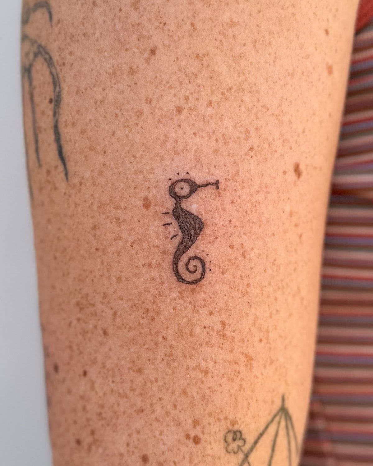 Tiny black seahorse tattoo on the upper arm, by Eli Inking, Bristol