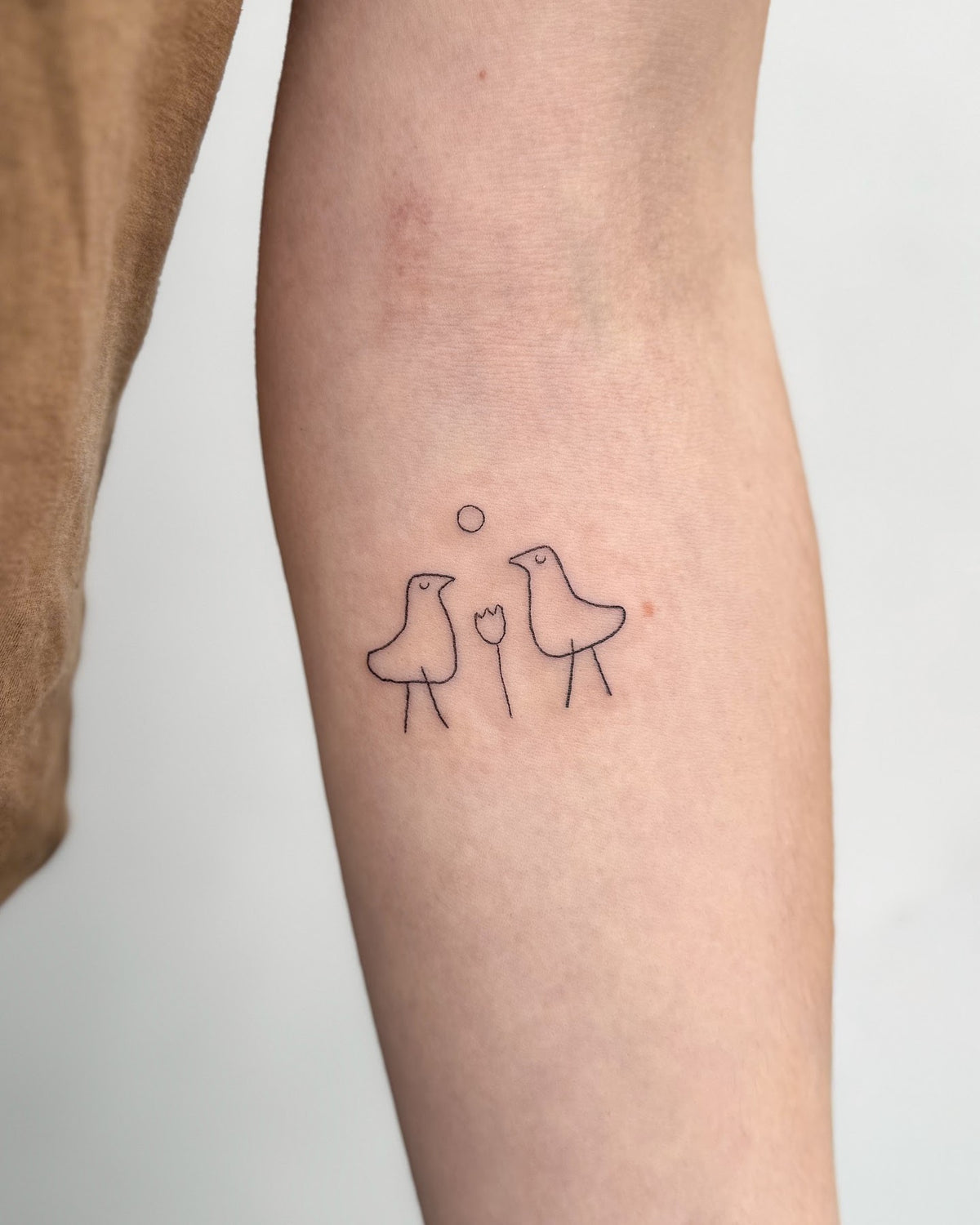 Small fine line tattoo of two little birds either side of a flower, on the inner forearm, by Eli Inking, Bristol
