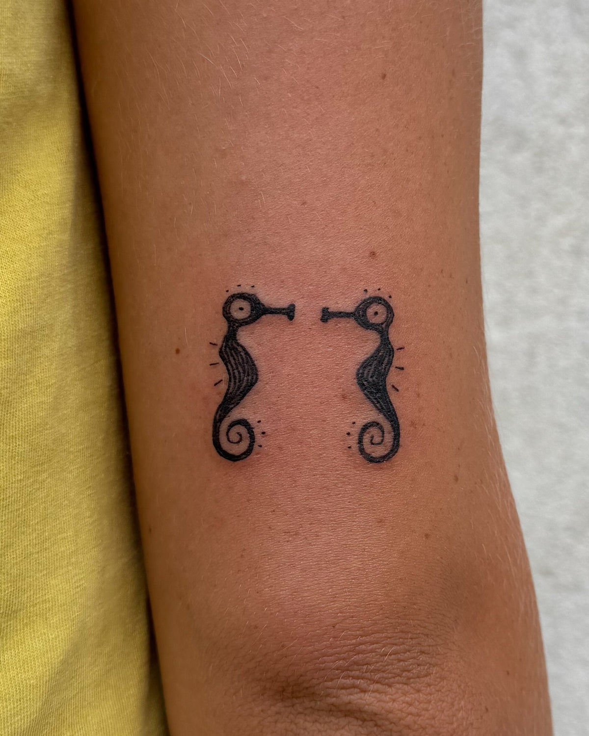 Small tattoo of two seahorses facing each other, on the back of the arm, by Eli Inking in Bristol