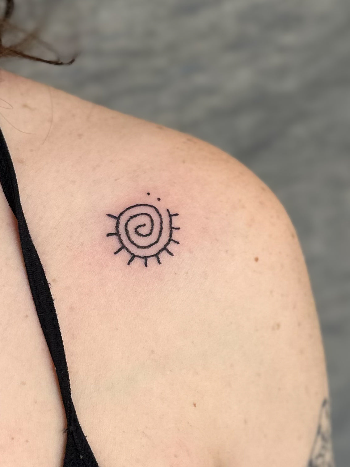 Small spiral sun tattoo on the shoulder, by Eli Inking