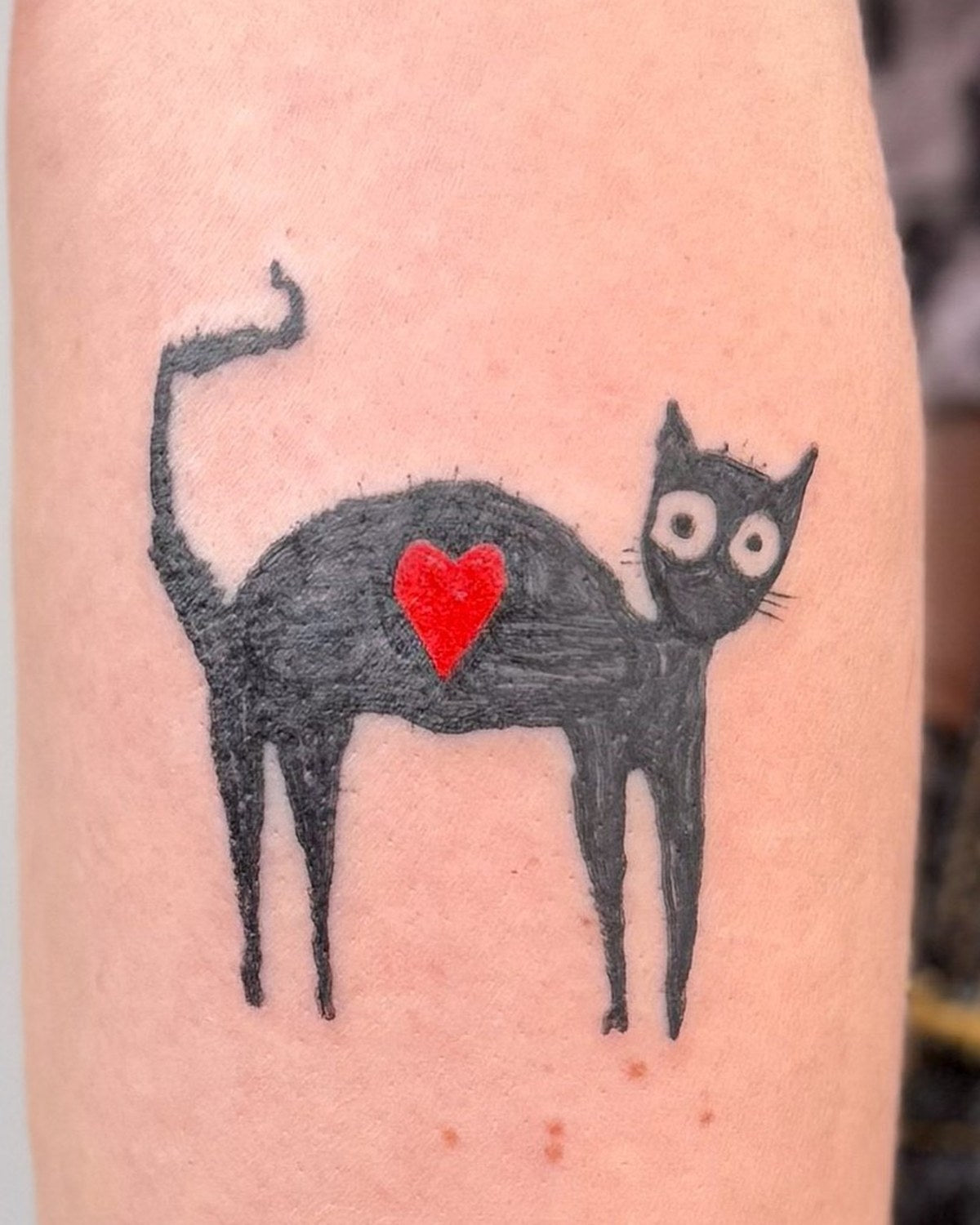 Black cat tattoo with a red heart by Eli Inking
