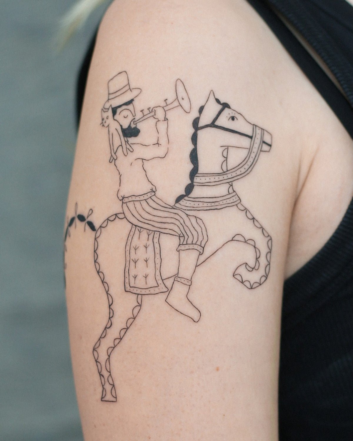 Folk style tattoo of a man in a hat playing a trumpet while riding a horse, on an upper arm, by Eli Inking in Bristol